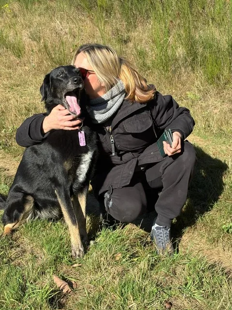 Steffi hockt auf einer Wiese und umarmt ihren schwarz-braunen Hund